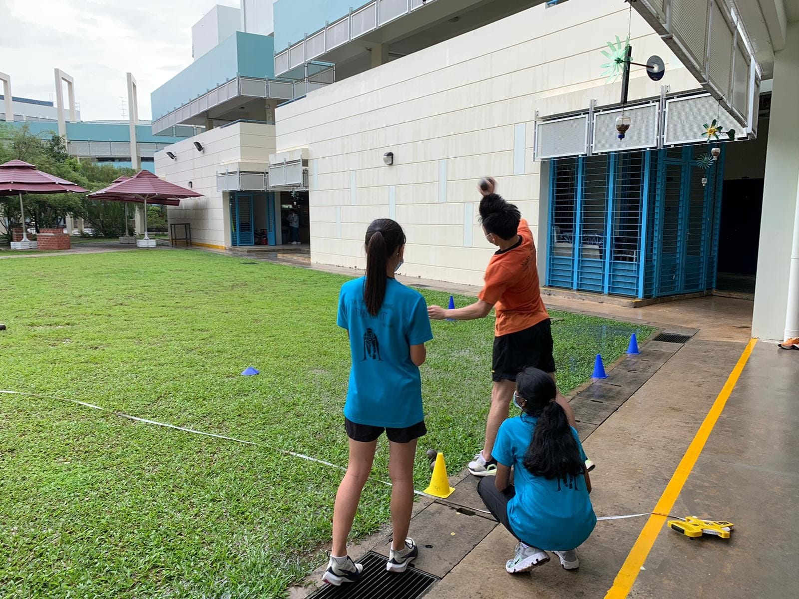Student participates in a shot put activity on a school field while peers observe and measure the throw.